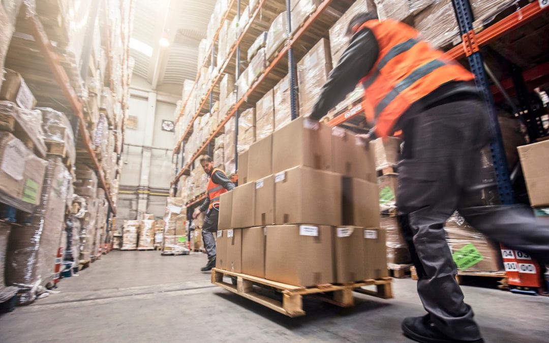 Two men moving boxes on a pallet inside a warehouse setting.
