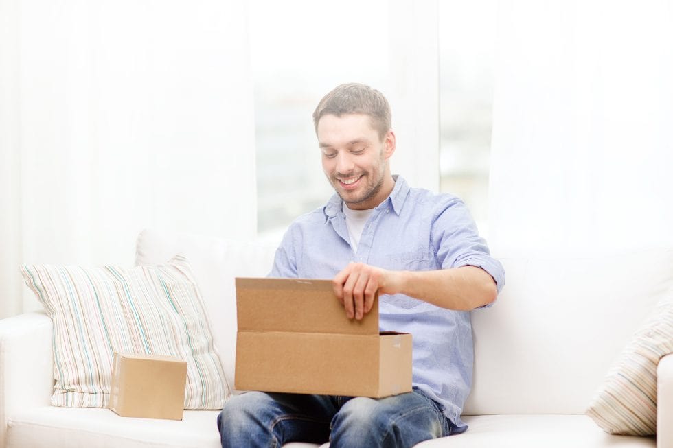 A man sitting on a couch opening a box.