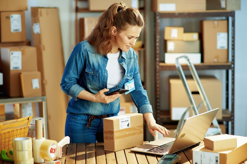 A woman using a laptop to prepare packages for shipping