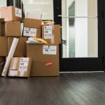 A large stack of cardboard boxes, envelopes and a cylinder are sitting inside a door of an office.